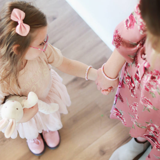 Two young girls holding hands, one with a plush toy, in a home setting.