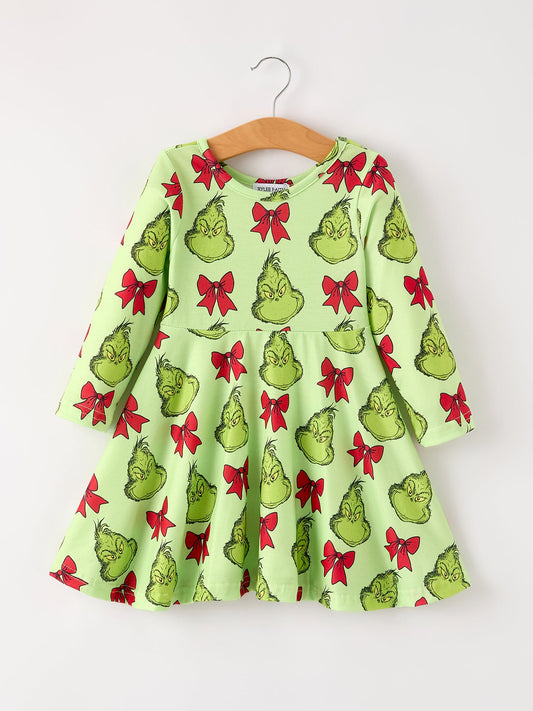Green dress with Grinch print and red bows on a hanger against a white background