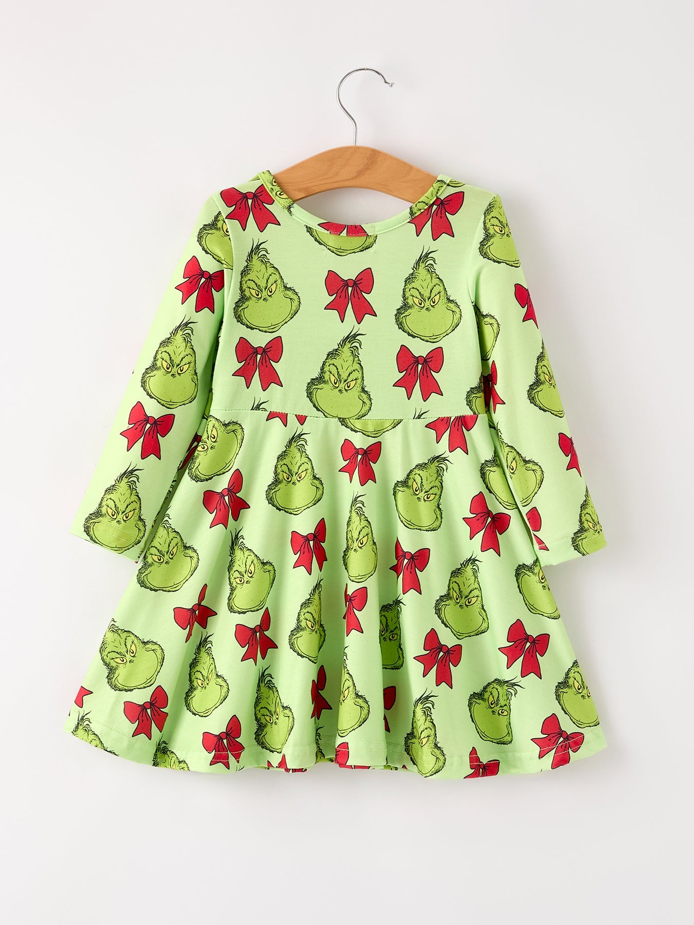 Green dress with Grinch print on a hanger against a white background
