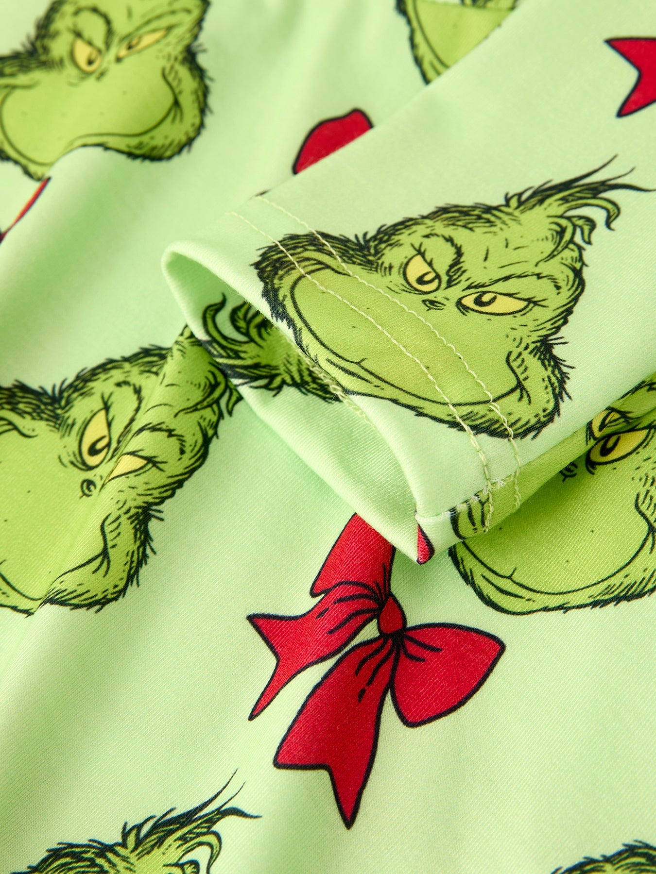 Close-up of fabric with Grinch pattern featuring green faces and red bows.