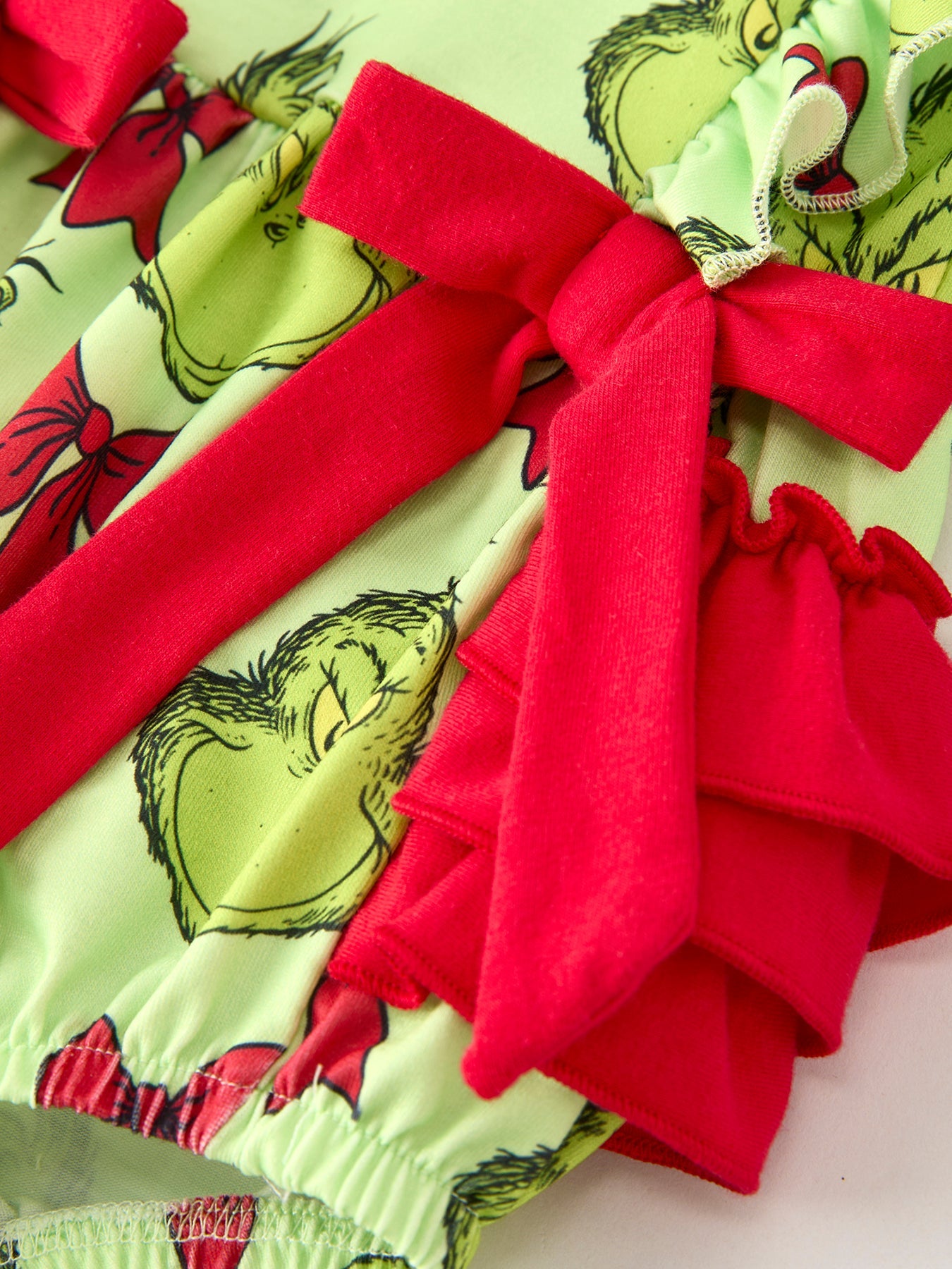Close-up of a festive fabric with red bows and a green character design.