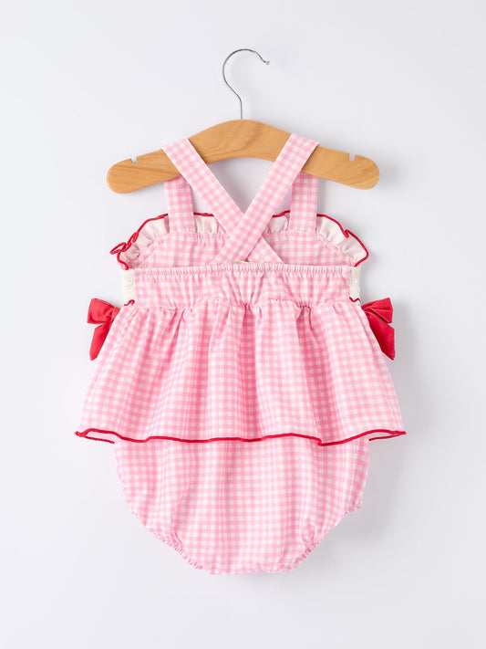 Pink gingham baby romper with red trim on a wooden hanger against a white background