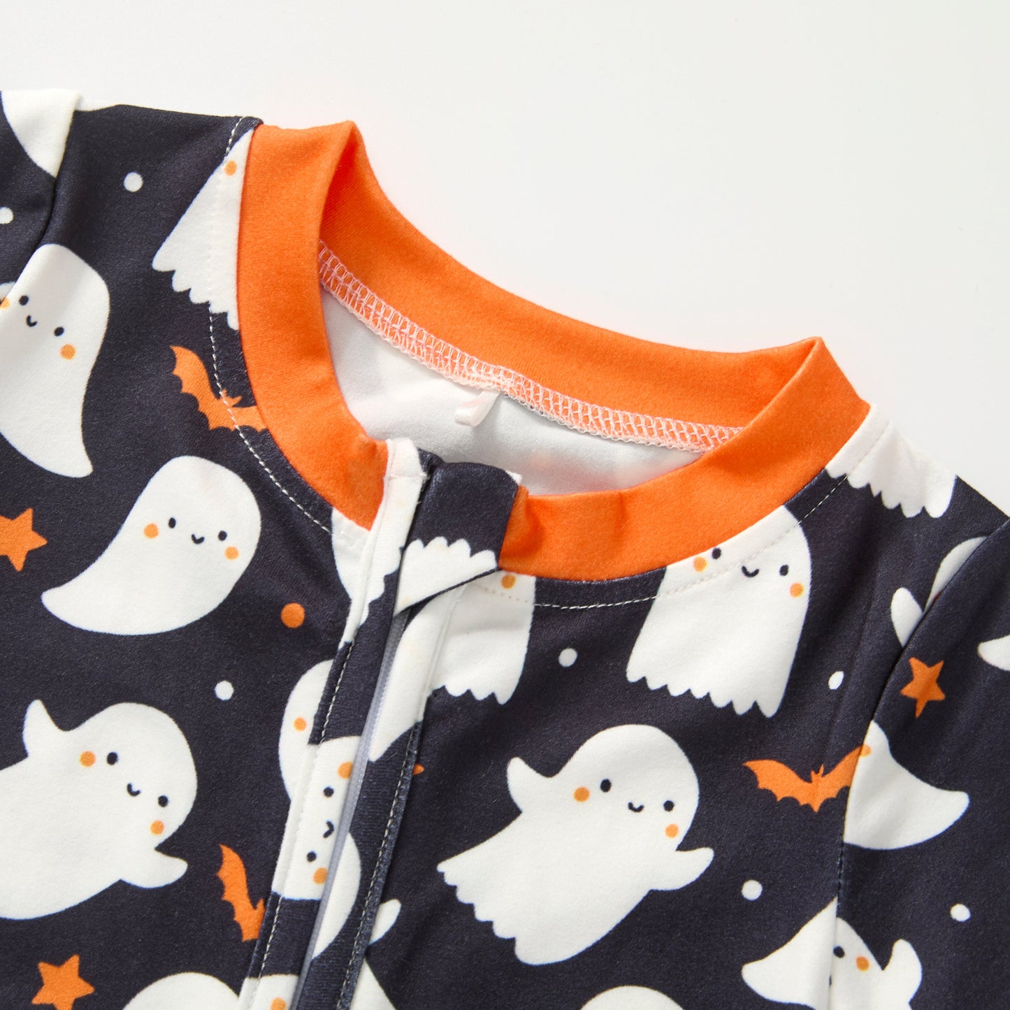 Close-up of a baby garment featuring a navy blue Halloween print with white ghosts, orange stars, and an orange ribbed collar.