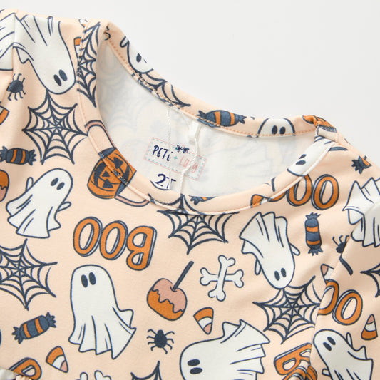 A close-up of a children's long-sleeve top with a Halloween print on a light peach background. The pattern features white ghosts, black spiderwebs, orange pumpkins, candy corn, and the word 'Boo' in orange.