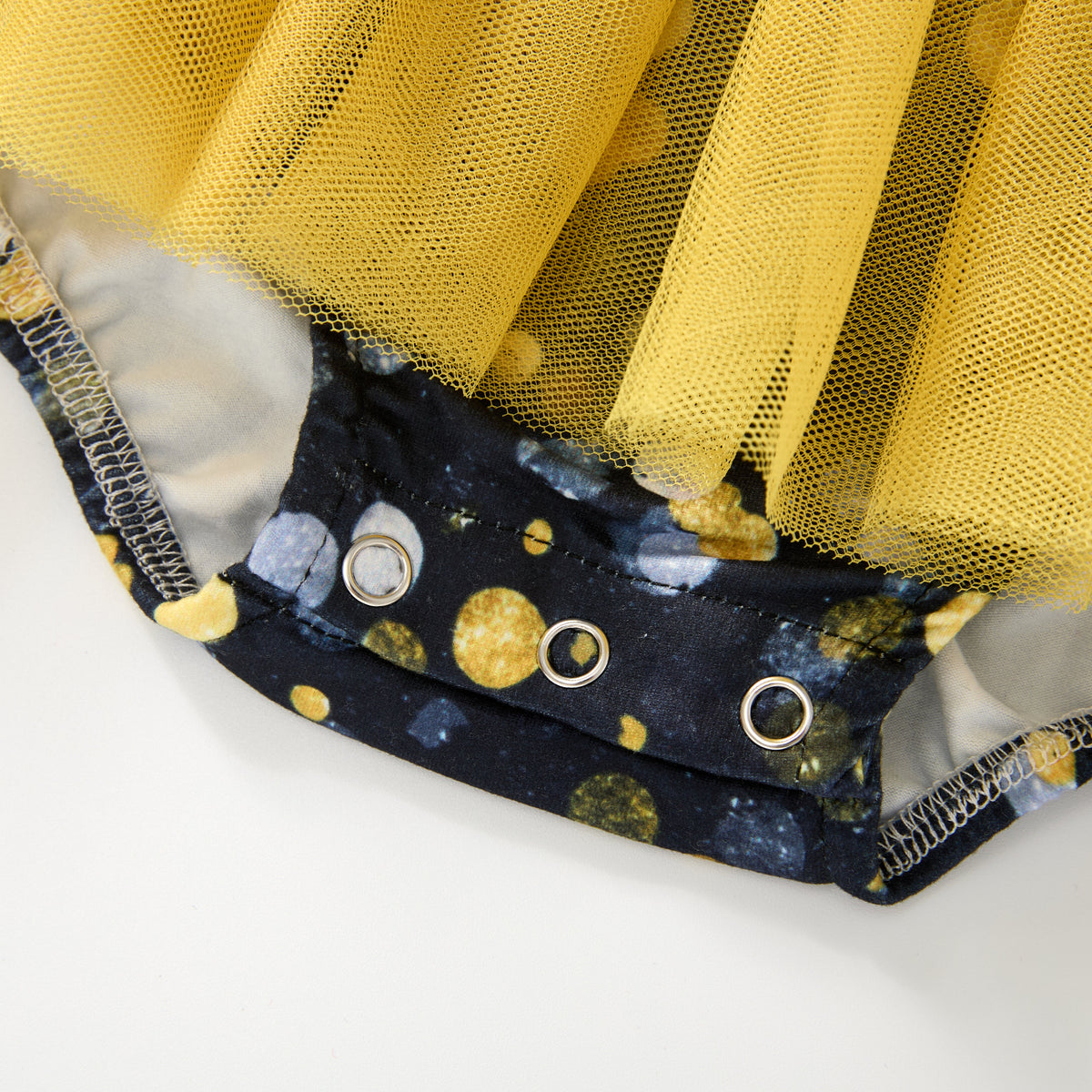Close-up of a yellow tulle skirt or tutu attached to a navy blue fabric waistband with gold polka dots and silver metal grommets, shown on a white background.