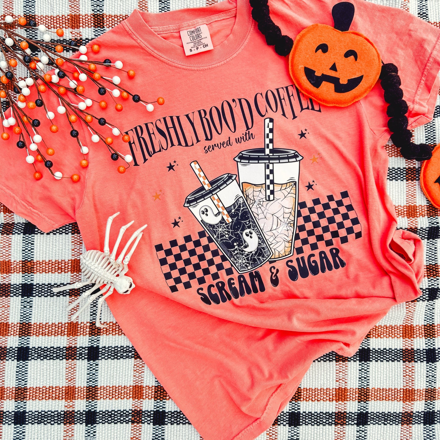 Pink t-shirt with Halloween-themed design on a plaid fabric background