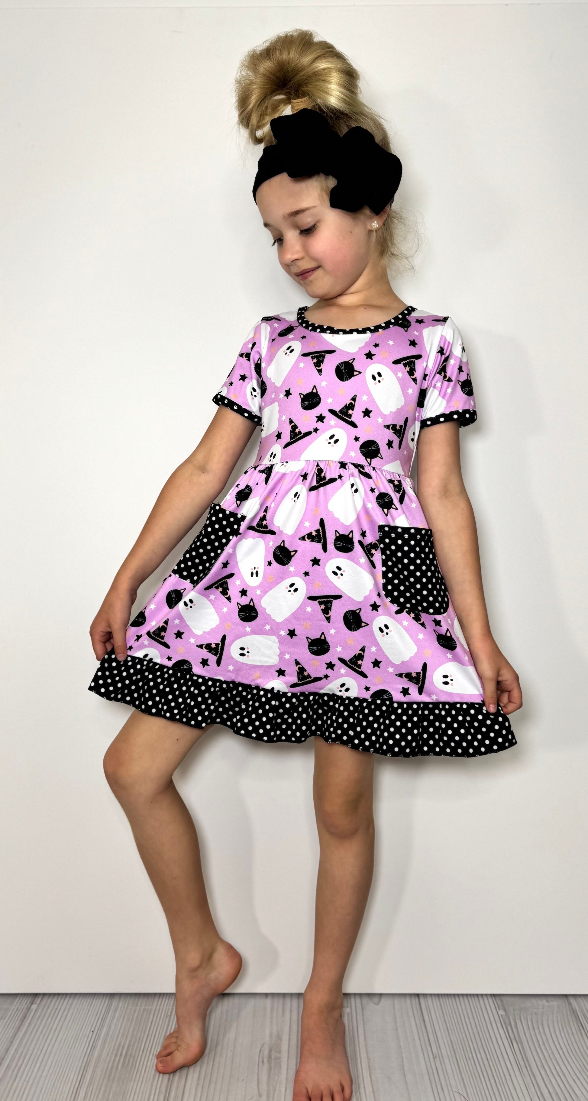 Young girl wearing a lavender dress with black cat & white ghost pattern on a white background