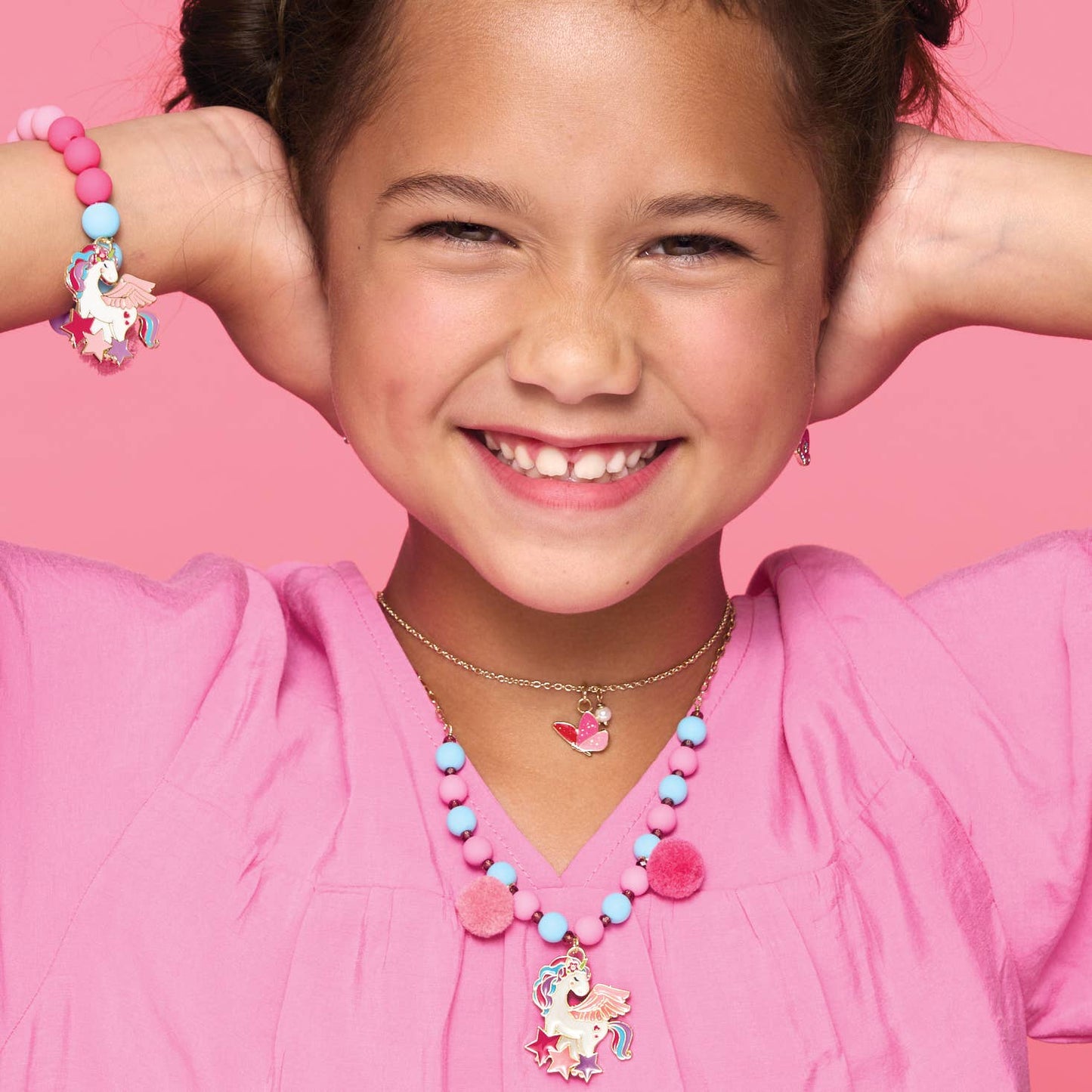 Young girl wearing a pink shirt and colorful jewelry against a pink background