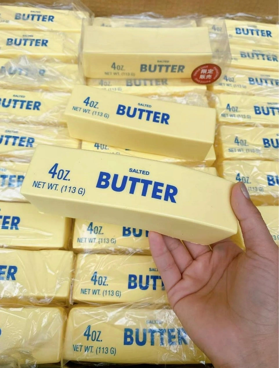 Hand holding a 4oz block of butter with more butter blocks in the background
