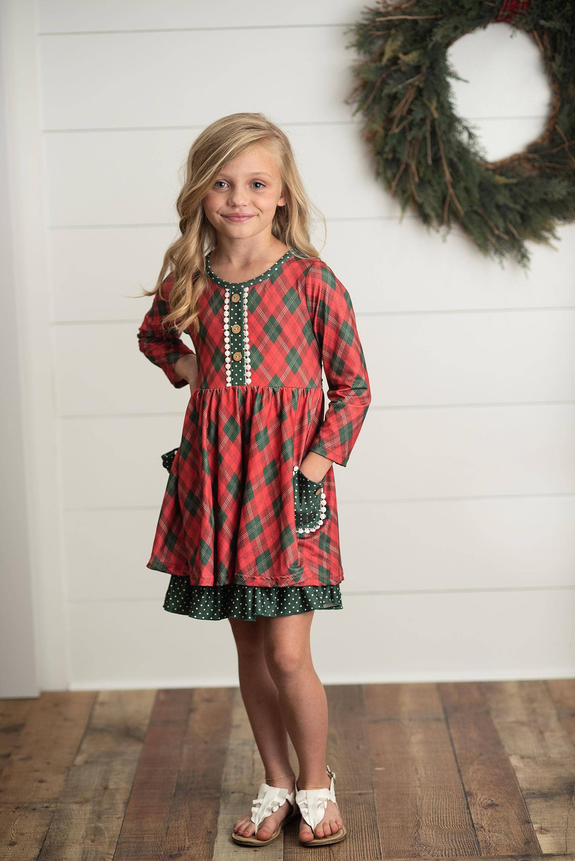 Young girl wearing a red plaid dress with a wreath in the background