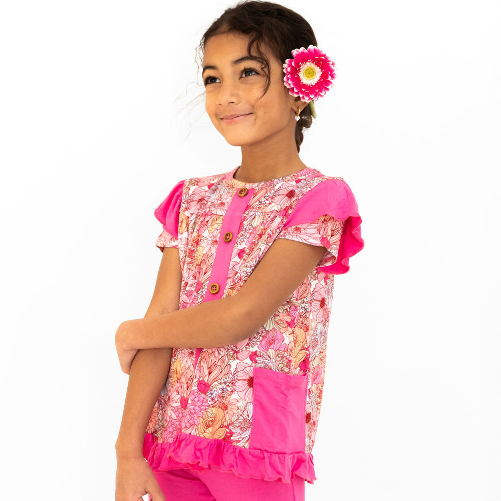 A girl wearing a pink floral peplum top with ruffled sleeves and matching leggings.