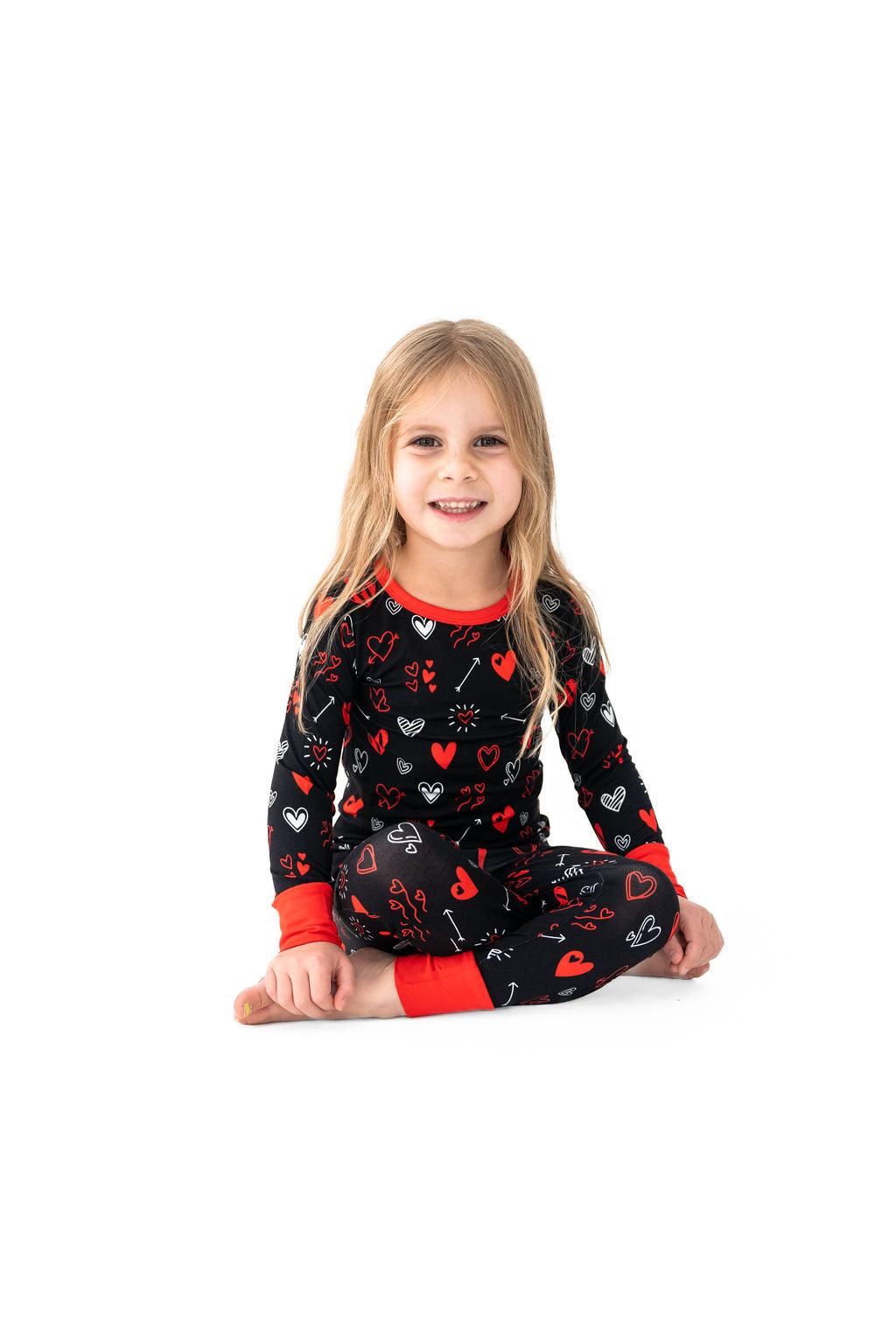 A child sitting and smiling, wearing a red and black heart-patterned pajama set.