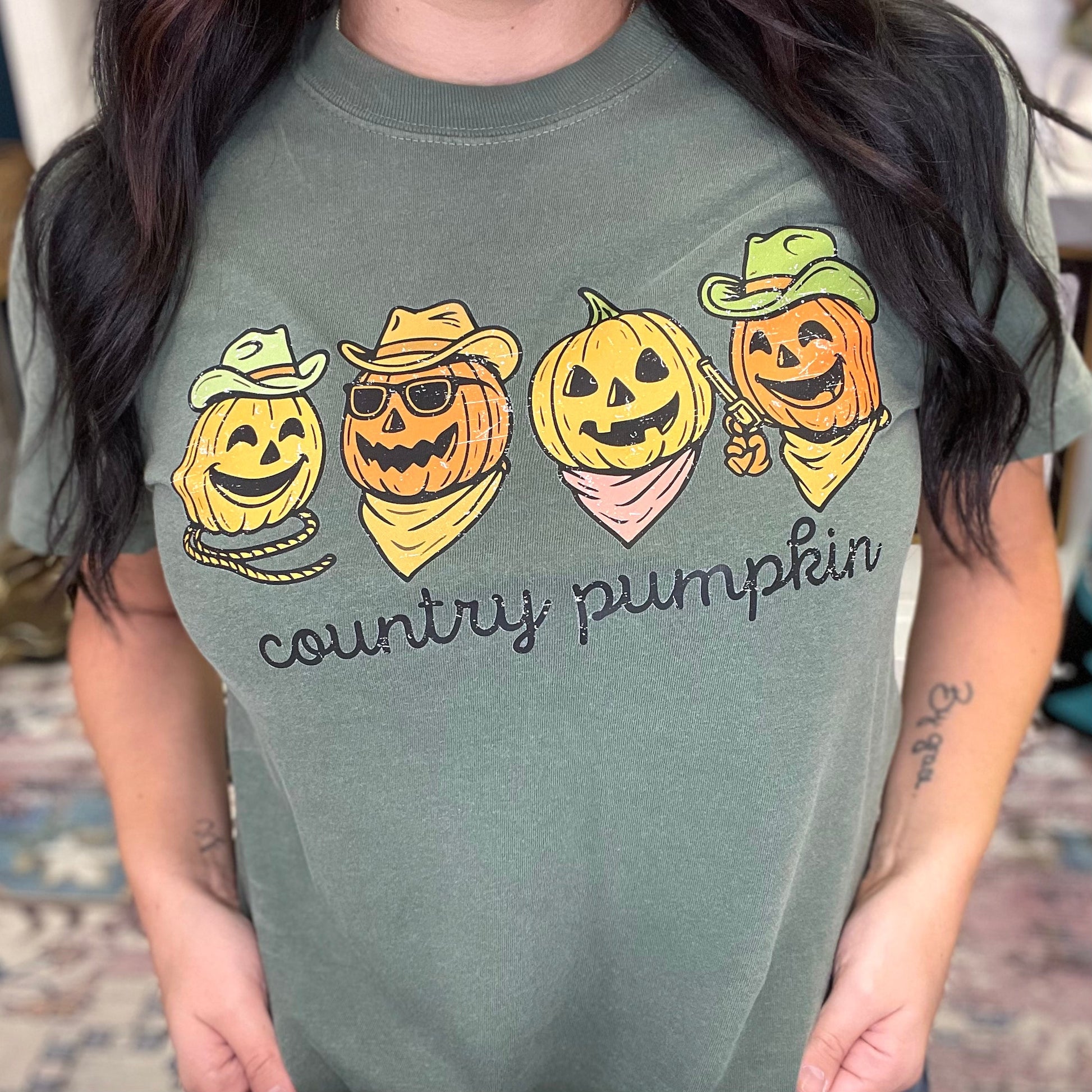 Person wearing a green t-shirt with 'country pumpkin' design featuring pumpkins in hats and bandanas.
