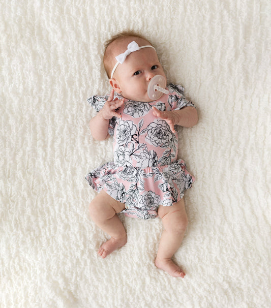 Baby in a floral romper with a pacifier on a white blanket