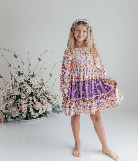 Young girl in a floral dress standing next to a floral arrangement on a white background