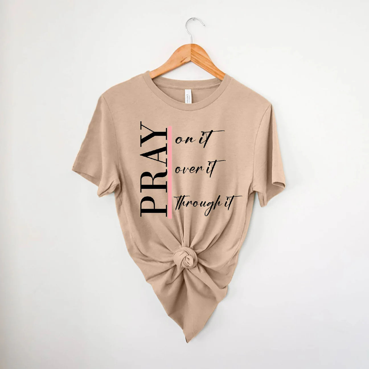 Beige t-shirt with 'PRAY on it, over it, through it' text on a hanger against a white background