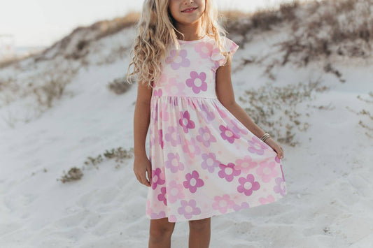 Young girl in a pink floral dress standing on sandy dunes.