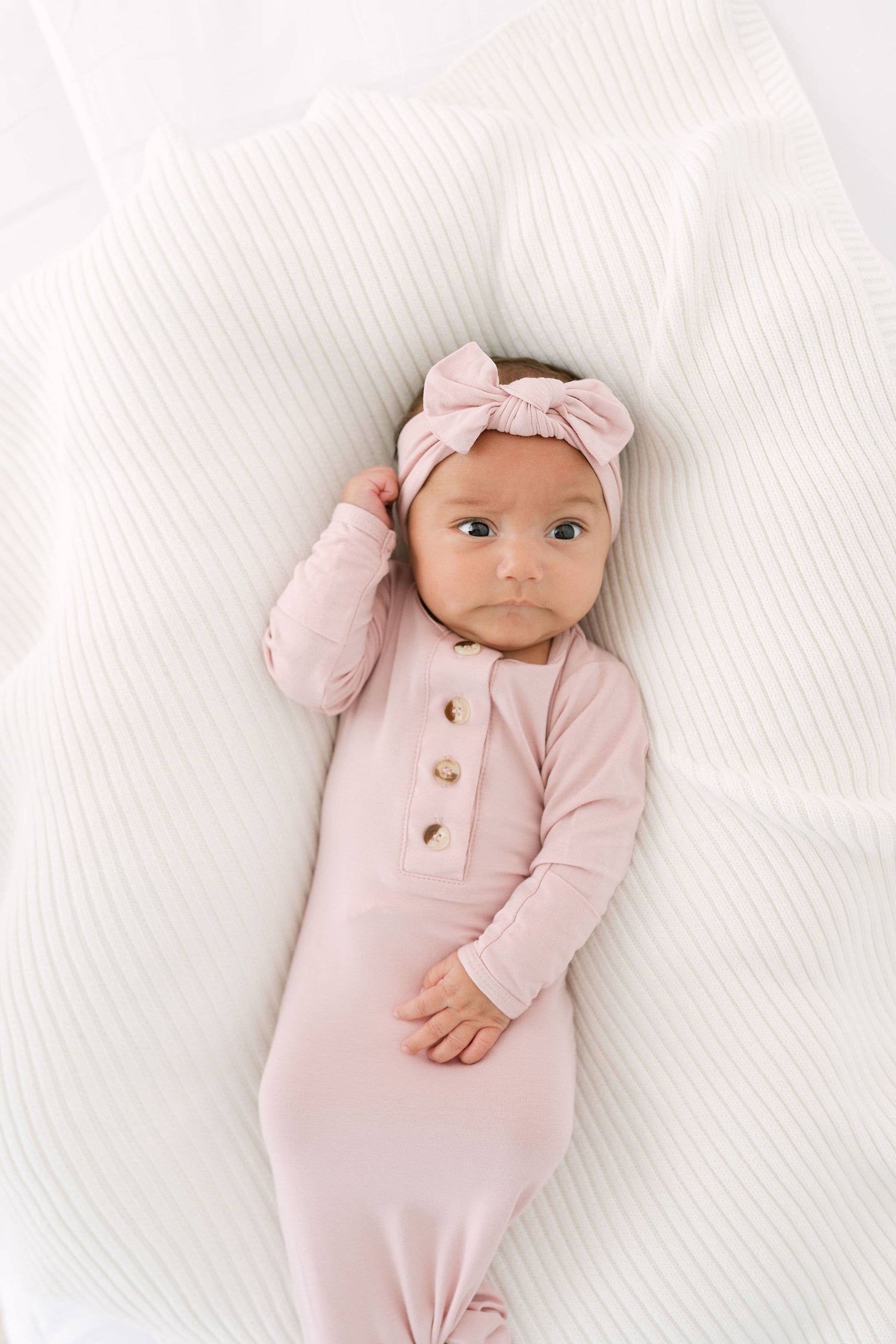 Baby wearing a pink outfit and headband lying on a white textured surface