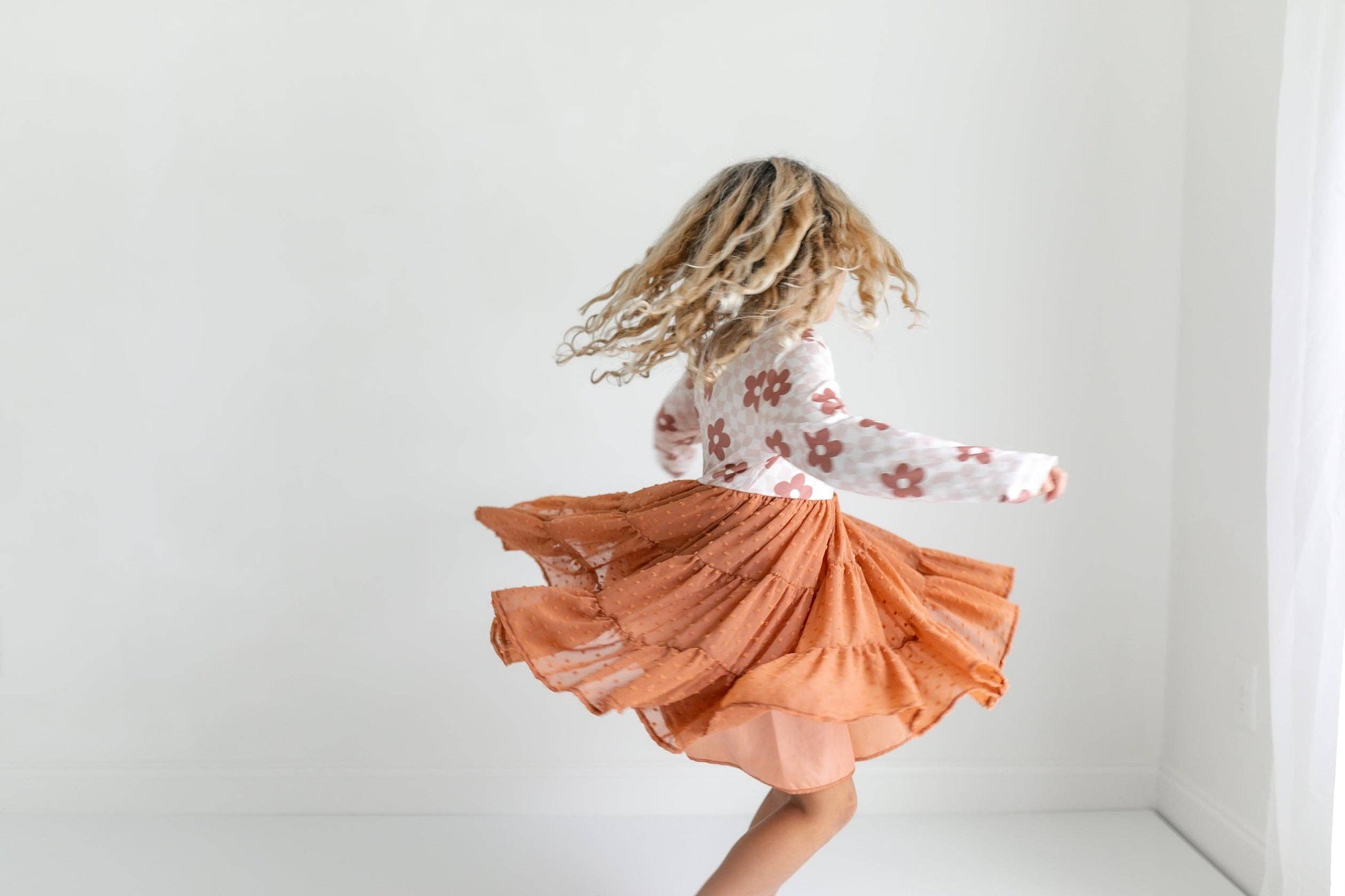 Person twirling in a floral top and orange skirt against a white background