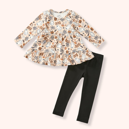 A toddler girl's two-piece outfit set featuring a long-sleeve peplum top with a beige, brown, and black Halloween-themed print, paired with solid black leggings, laid flat on a light cream background.