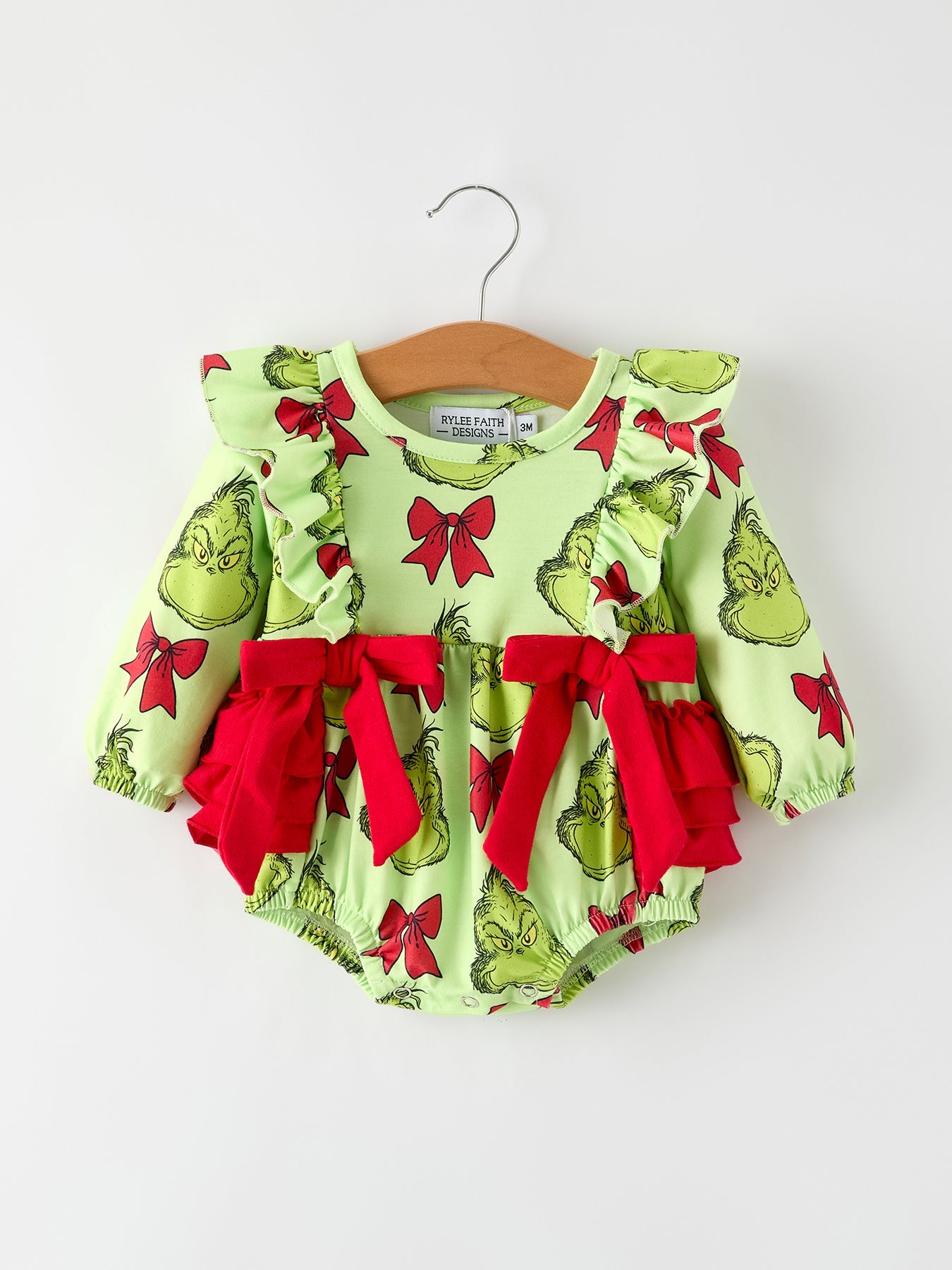 Green baby romper with red bows on a hanger against a white background