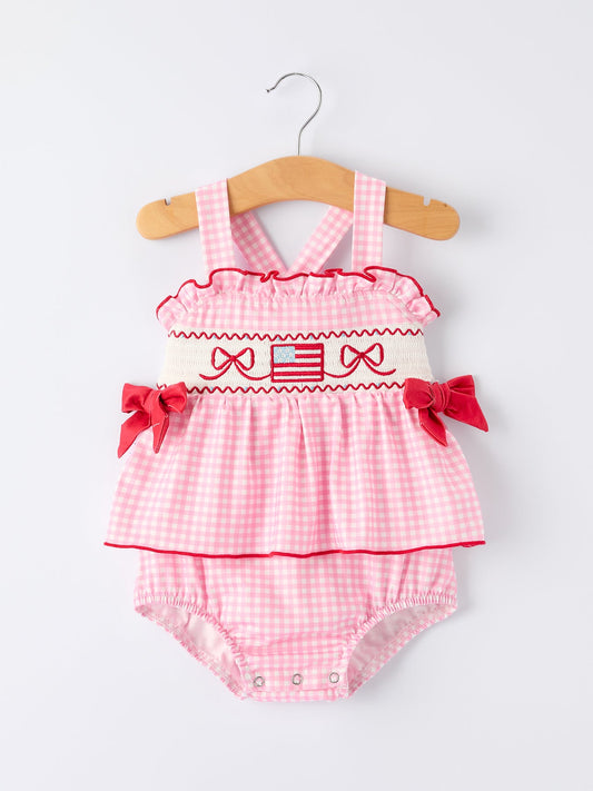 Pink checkered baby romper with ruffles and bows on a hanger against a white background