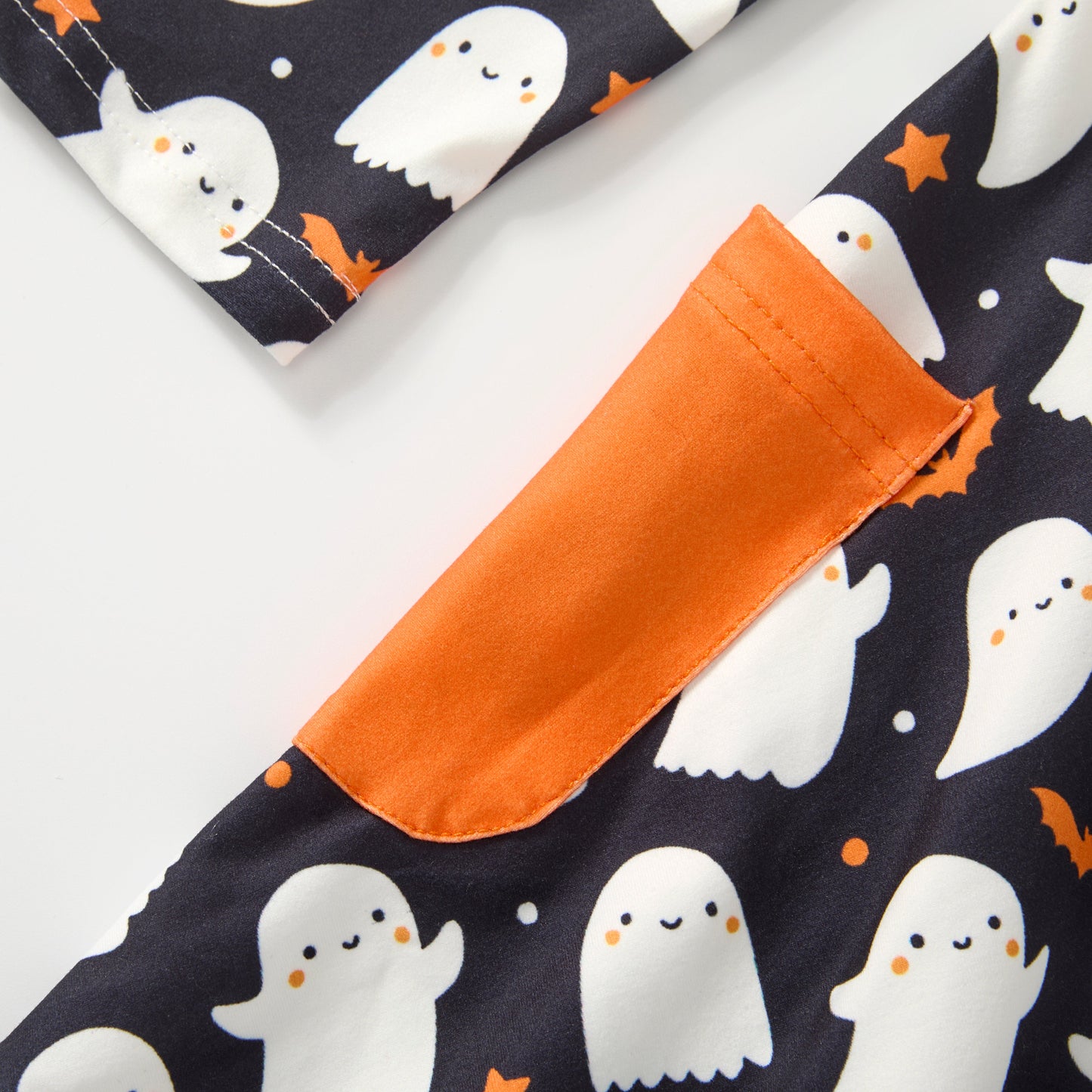 Close-up of a Halloween-themed dres featuring a black background with white cartoon ghosts, orange bats & stars, and a contrasting orange pocket.