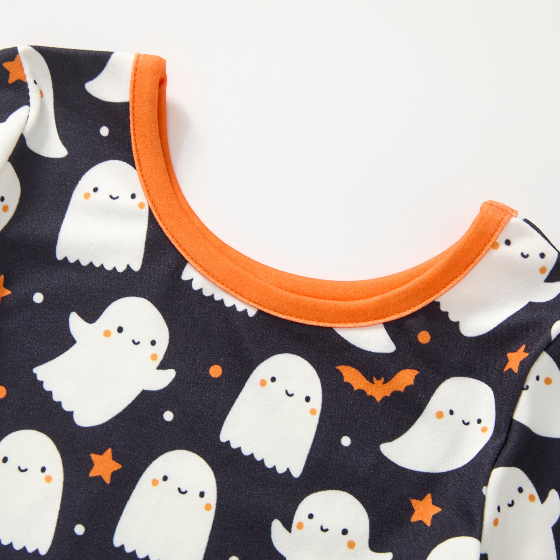 Close-up of a Halloween dress  featuring a black Halloween print with cute white ghosts, orange stars, and bats, finished with a bright orange ribbed crew neck.