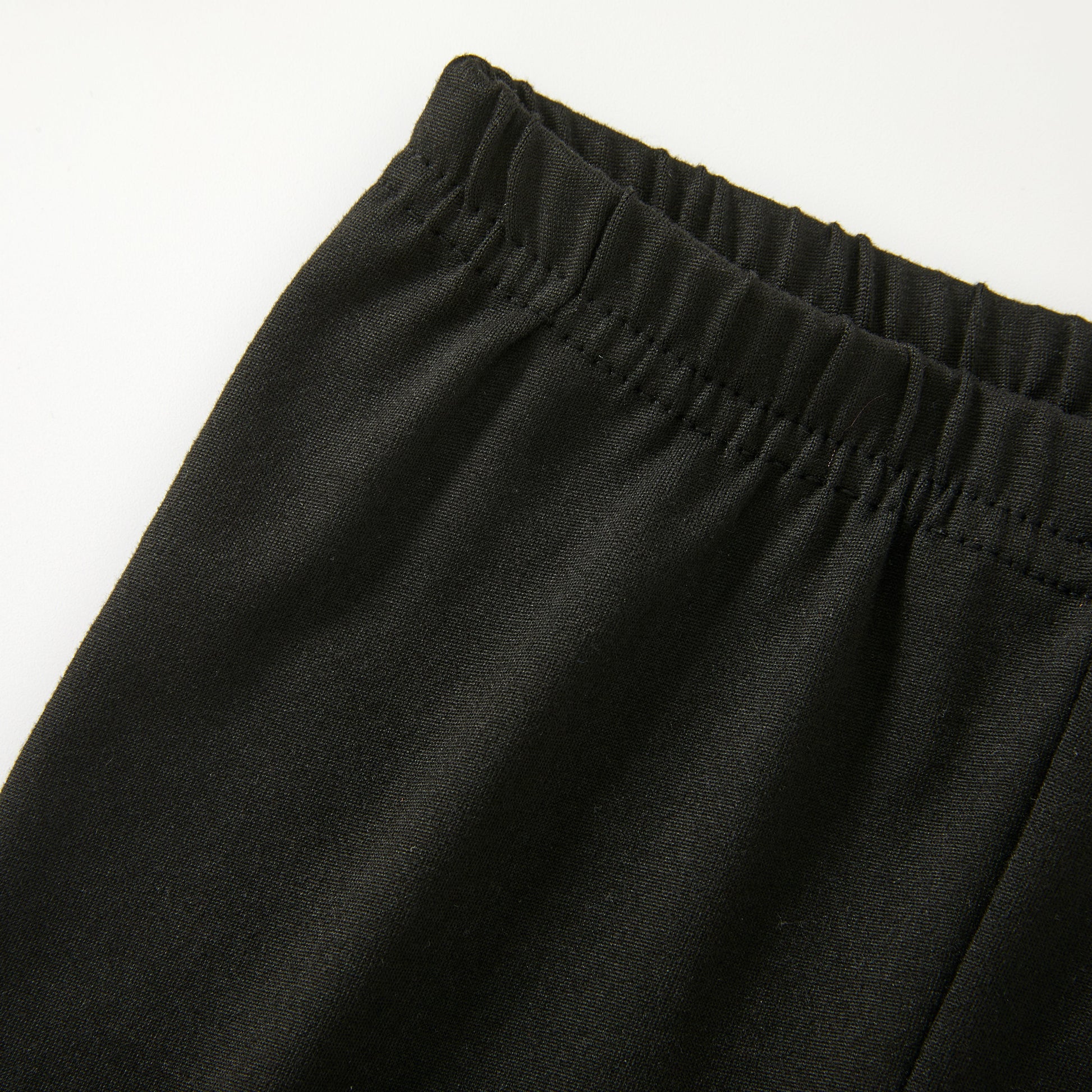 Close-up of the black elastic-waist pants on a plain white background.