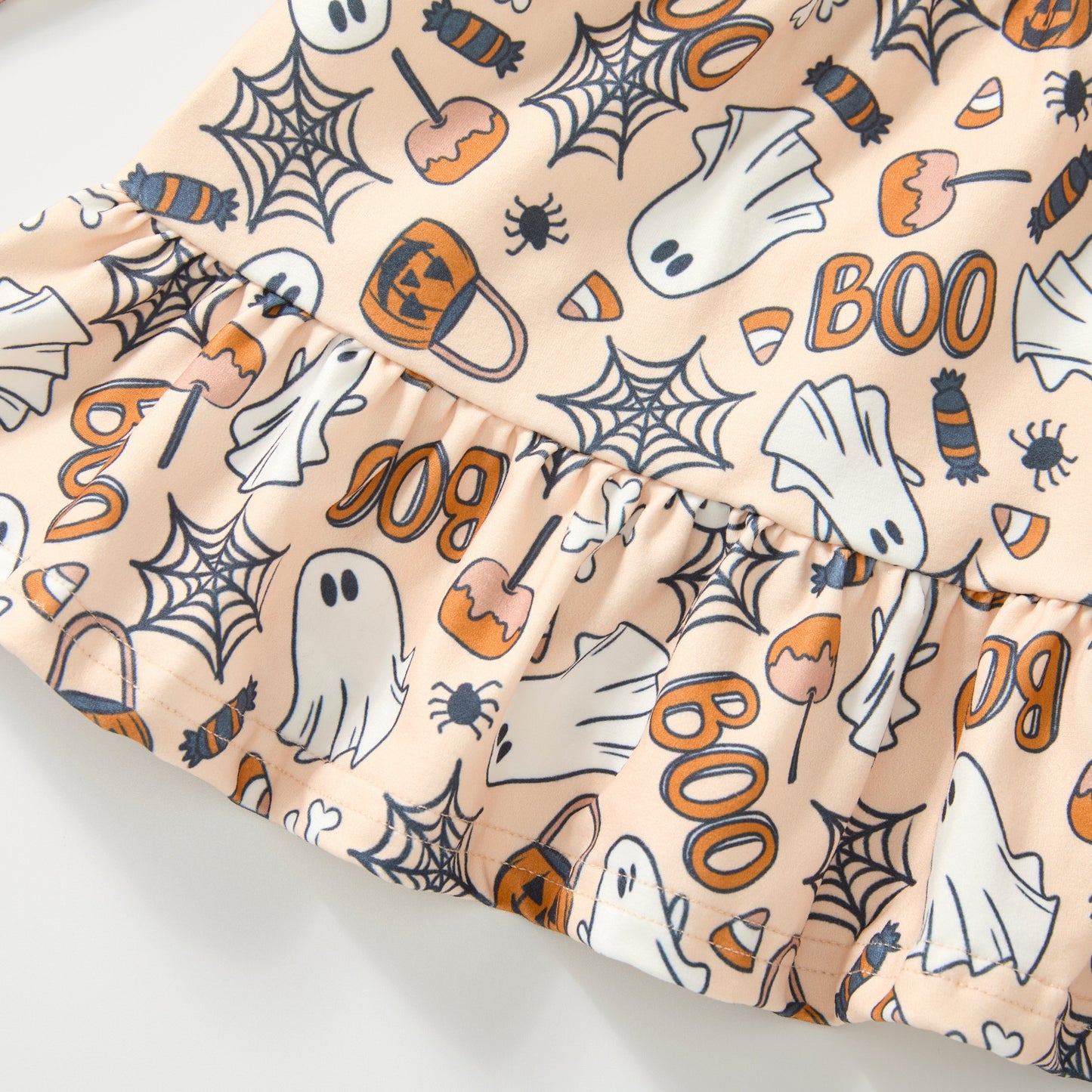 A close-up of a ruffled fabric trim featuring a Halloween print with ghosts, spiders, candy corn, pumpkins, and 'BOO' text on a light peach background.