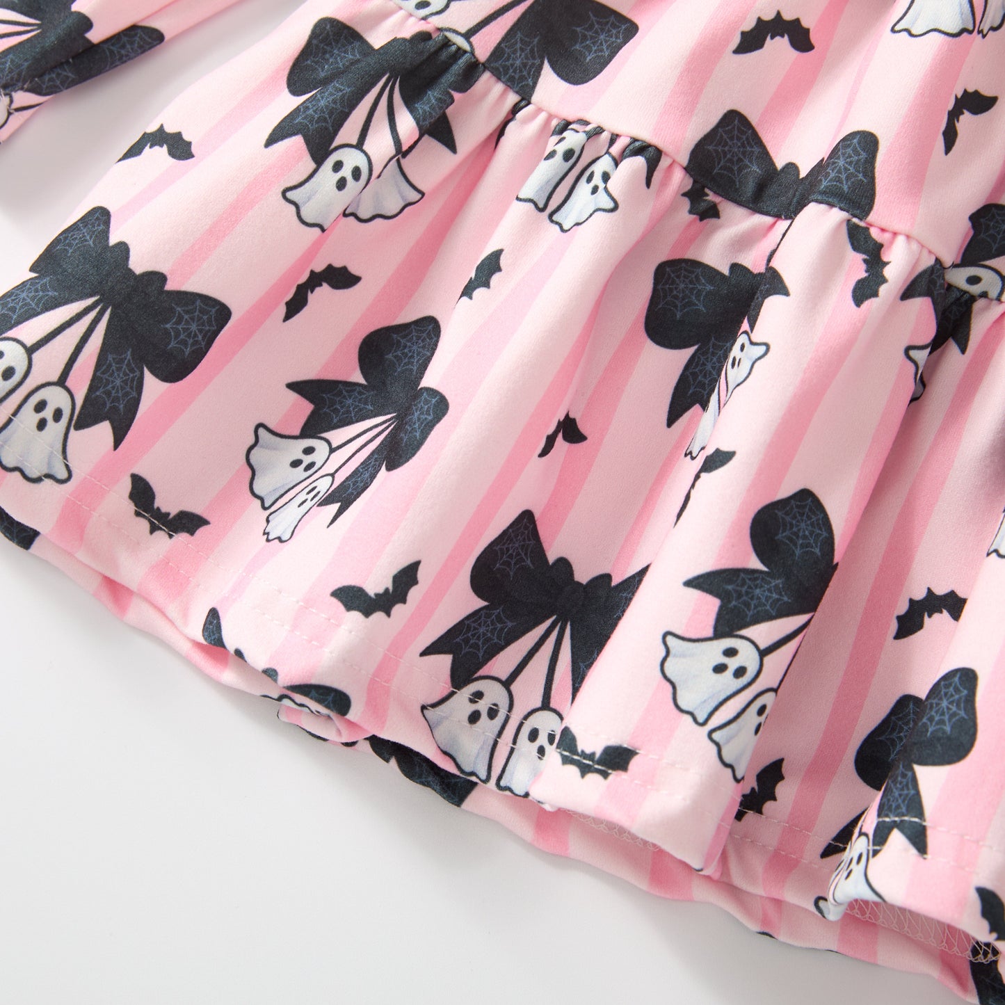 A close-up of a pink striped garment with a Halloween print featuring black bows, white ghosts, bats, and small black spider silhouettes.