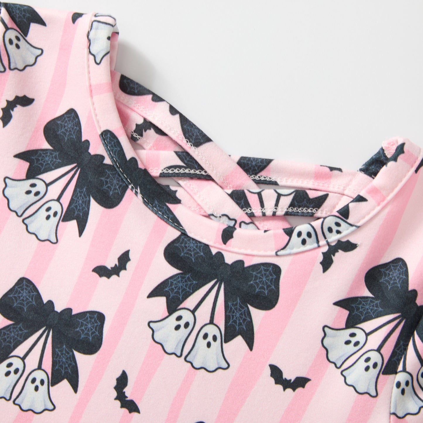 A close-up of a pink striped garment with a Halloween print featuring black bows, white ghosts, and small black bats.