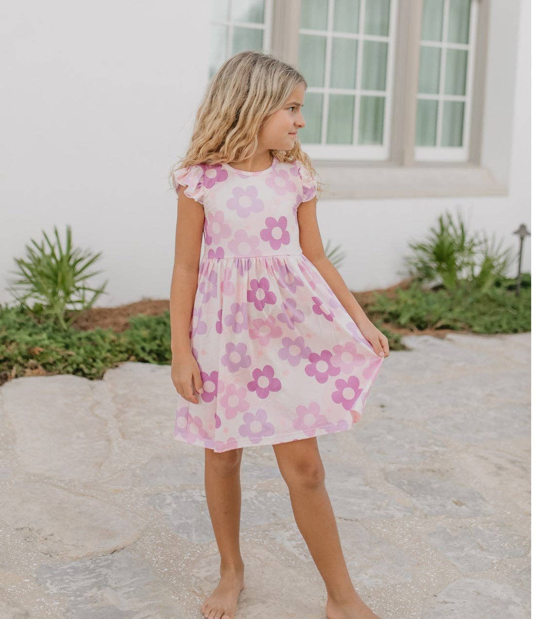 Young girl wearing a pink floral dress standing outdoors.