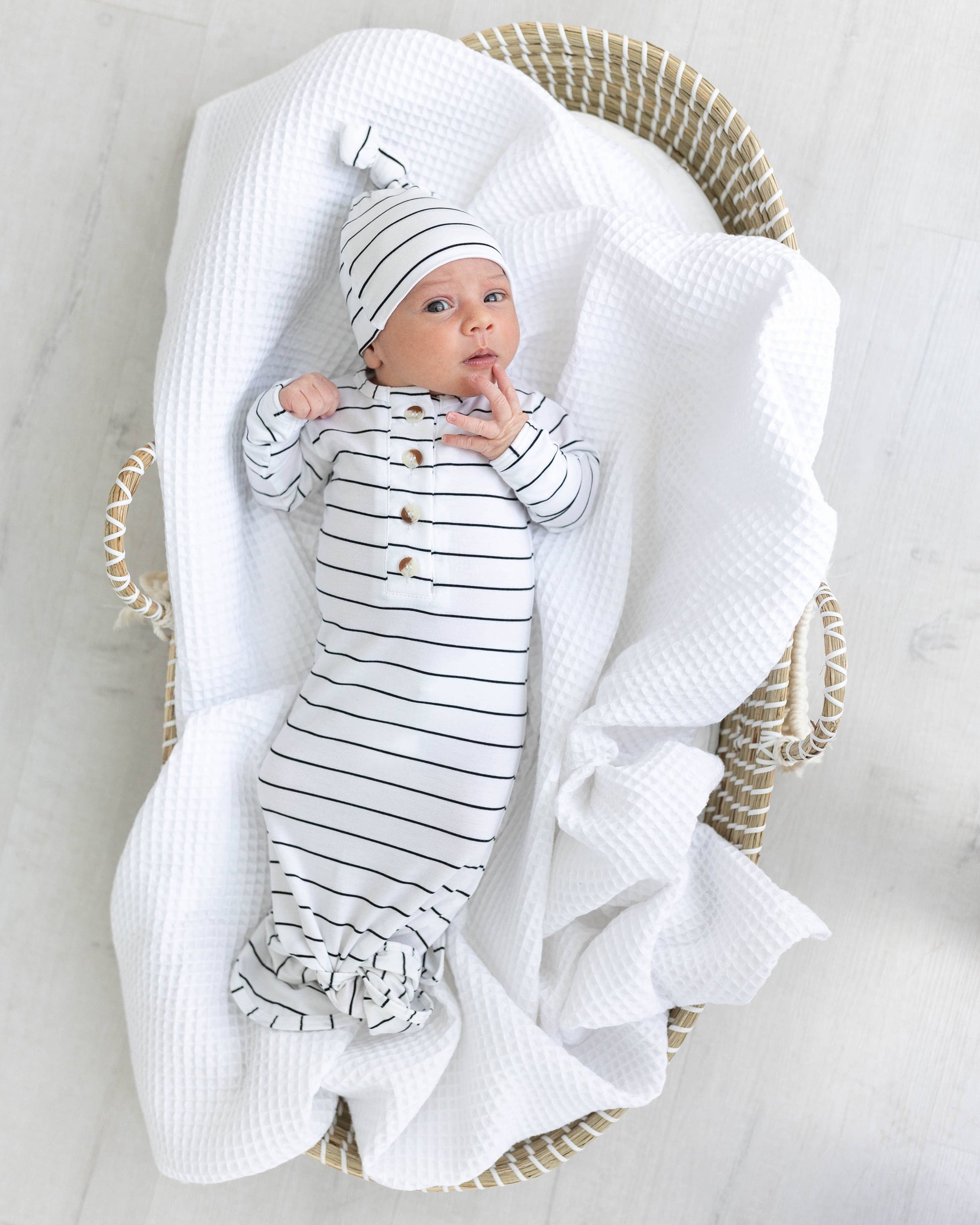 Newborn baby in a striped outfit and hat, wrapped in a white blanket, sitting in a wicker basket.