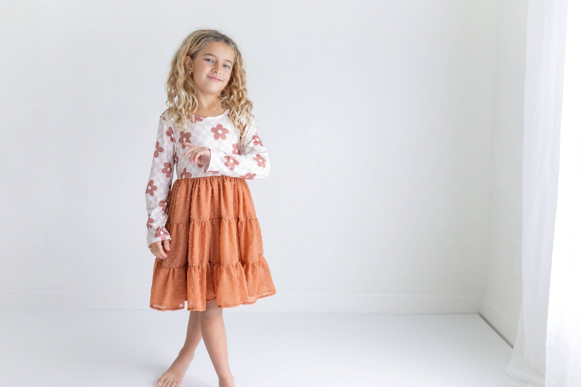 Young girl wearing a floral top and rust-colored skirt on a white background