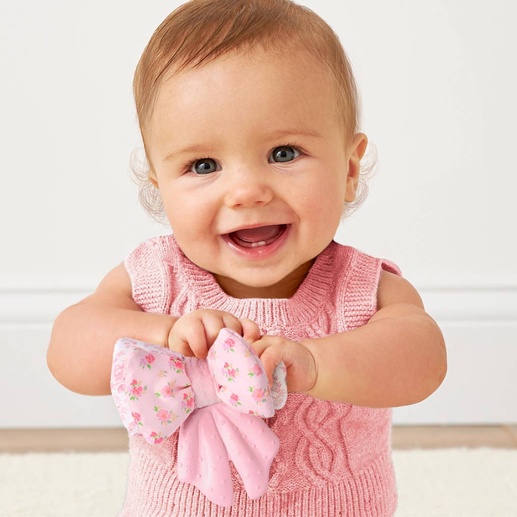 Baby in a pink outfit holding a floral bow against a white background