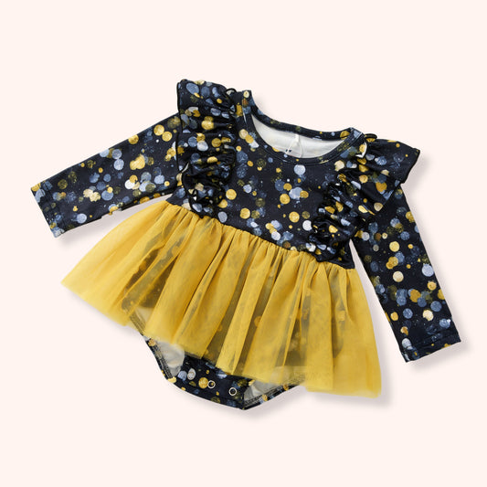 A baby girl's long-sleeve romper with a navy blue base covered in gold, yellow, and white polka dots, featuring a ruffled neckline and a layered yellow tulle tutu skirt.