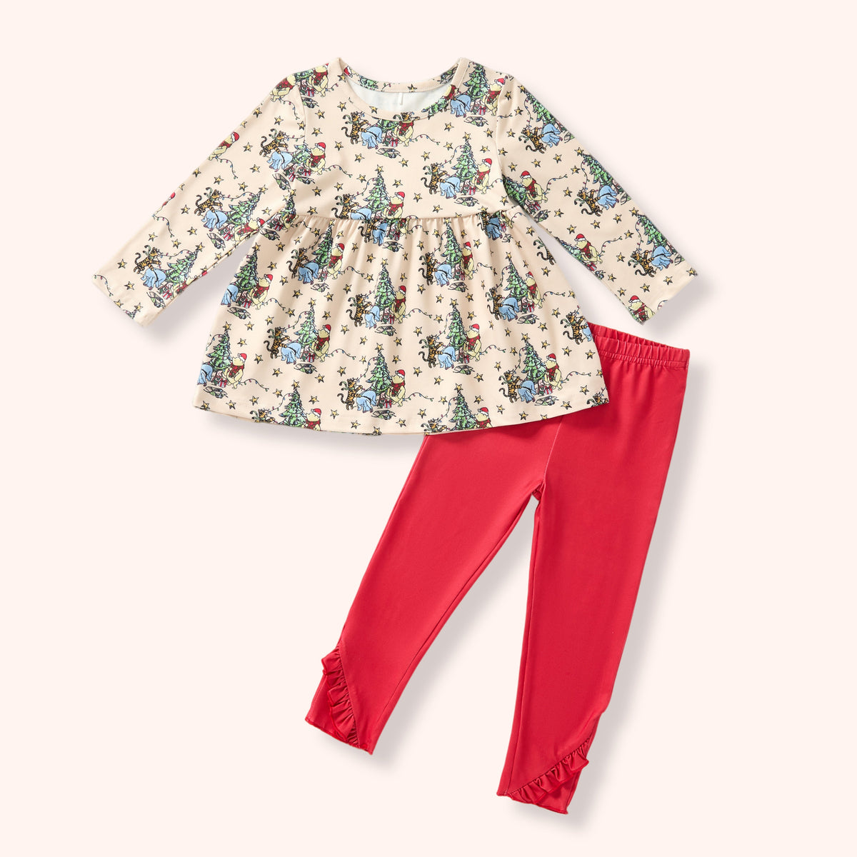 A toddler girl's two-piece outfit set featuring a long-sleeve cream-colored top with a festive Christmas tree print and solid bright red leggings with ruffled cuffs, laid flat on a light cream background.