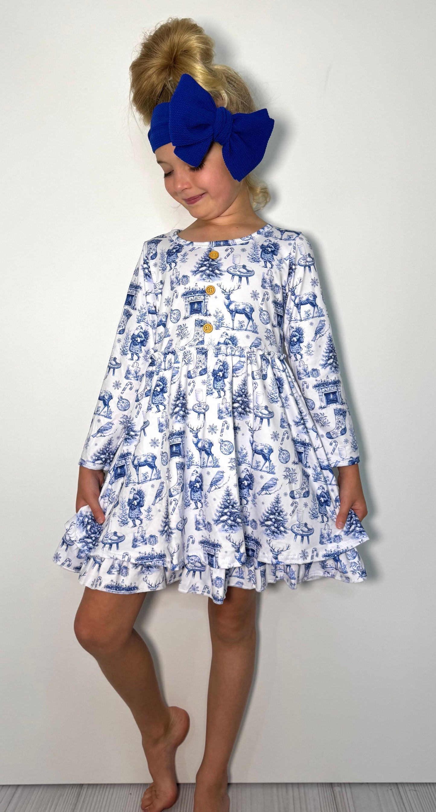 Child wearing a blue and white dress with long sleeves and a large blue bow on a plain background