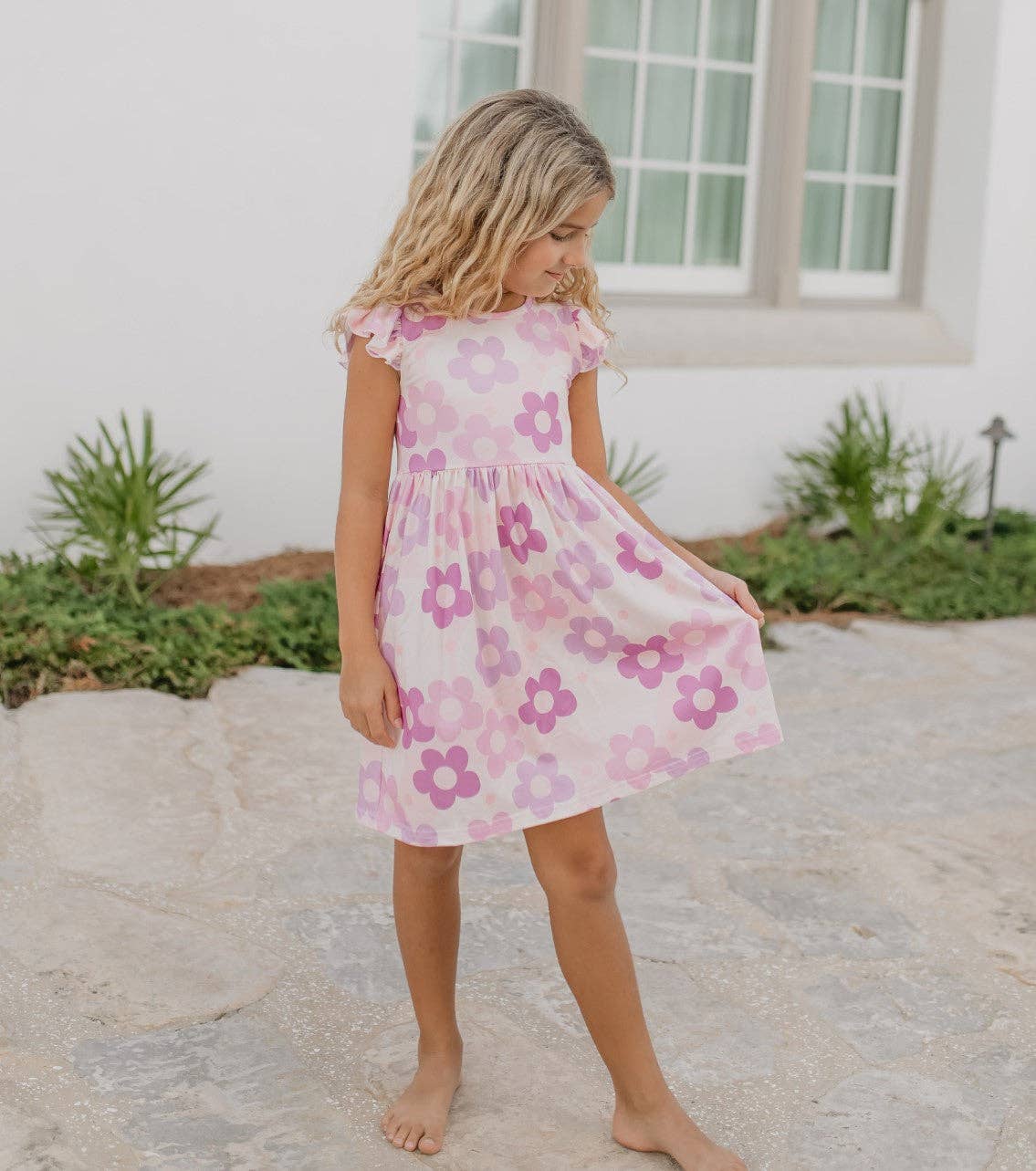 Young girl wearing a pink floral dress standing outdoors on a stone path.