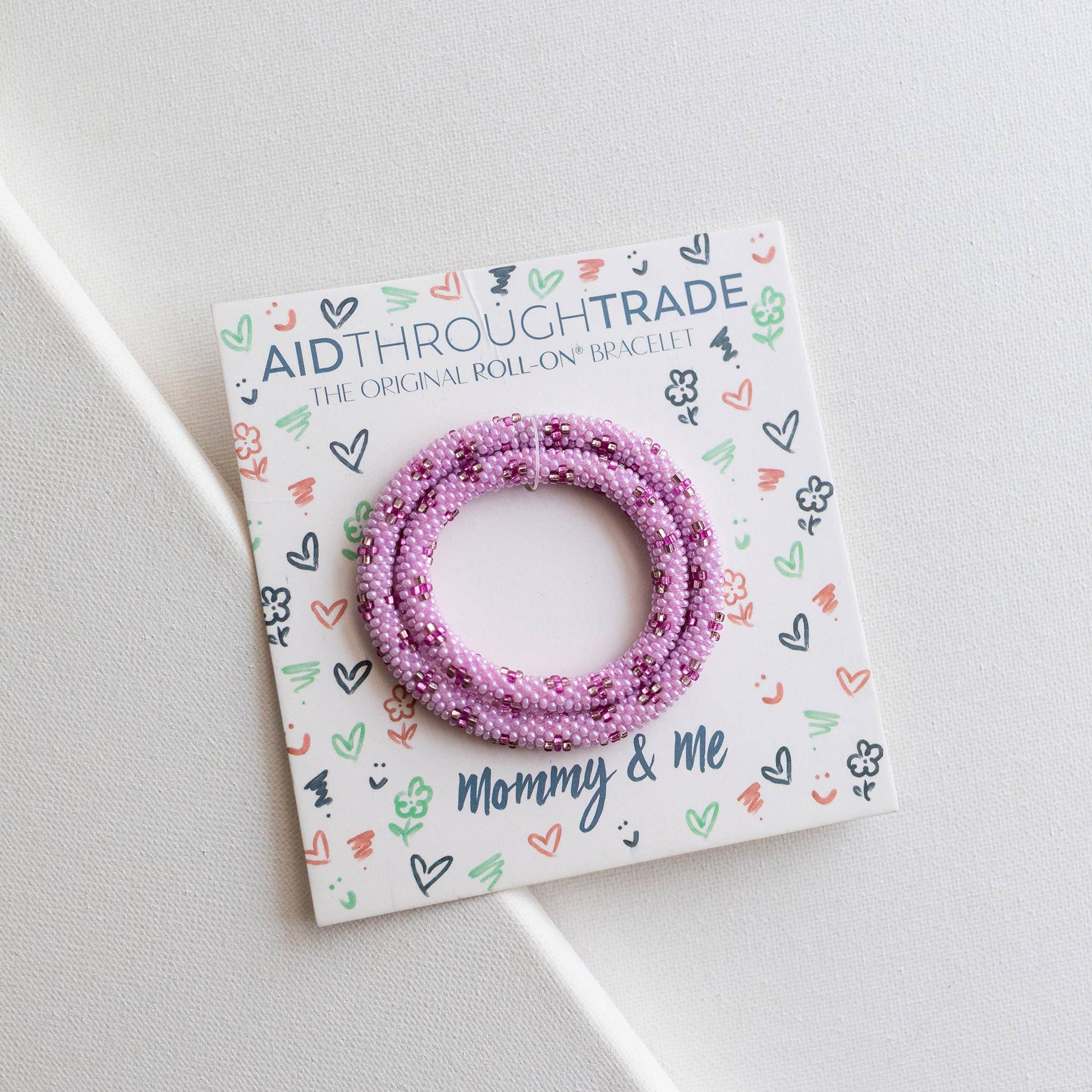 Pink beaded bracelet on a 'Aid Through Trade' branded card with decorative elements.
