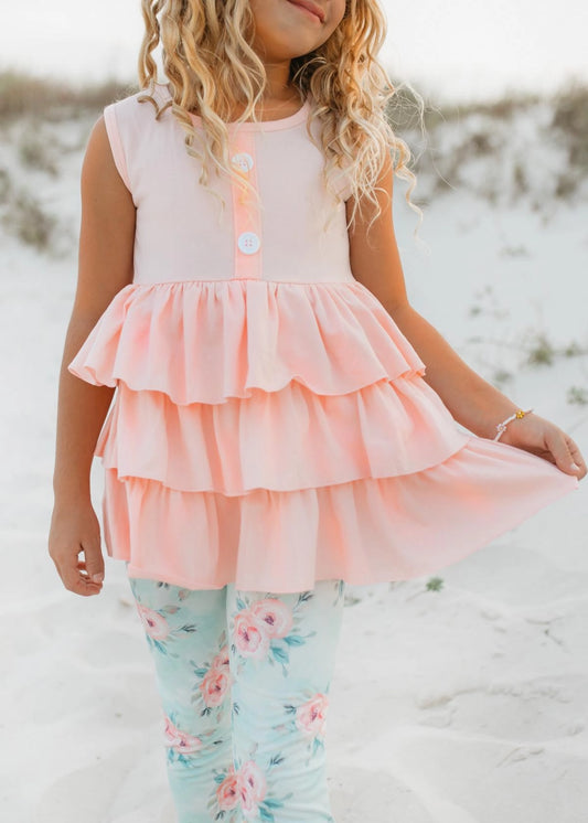 Child wearing a pink layered dress with floral pants on a sandy background