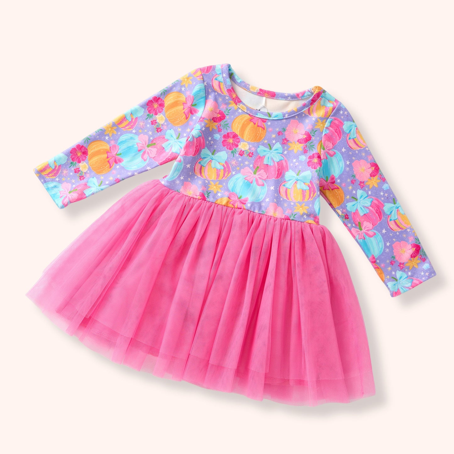 A toddler girl's long-sleeve dress with a bright pink tulle skirt and a purple patterned bodice featuring colorful pumpkins and flowers, shown on a light cream background.
