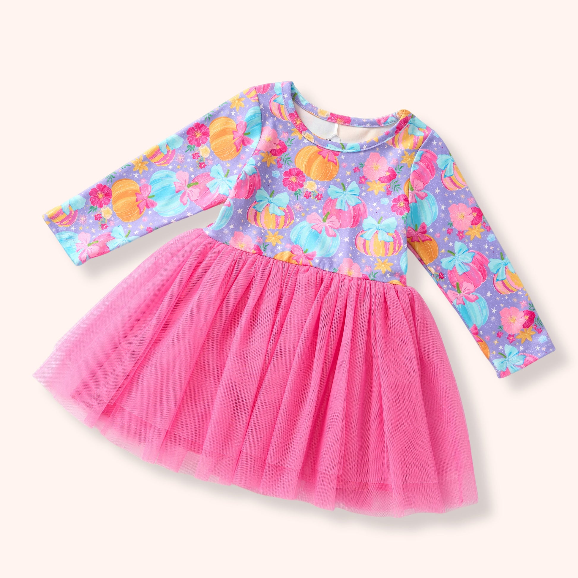A toddler girl's long-sleeve dress with a bright pink tulle skirt and a purple patterned bodice featuring colorful pumpkins and flowers, shown on a light cream background.