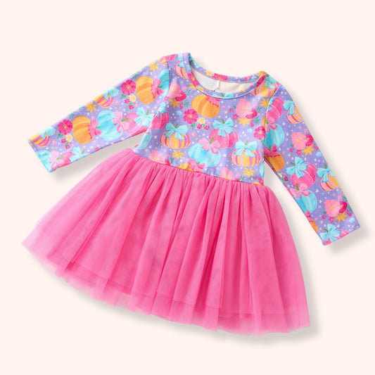 A toddler girl's long-sleeve dress with a bright pink tulle skirt and a purple patterned bodice featuring colorful pumpkins and flowers, shown on a light cream background.