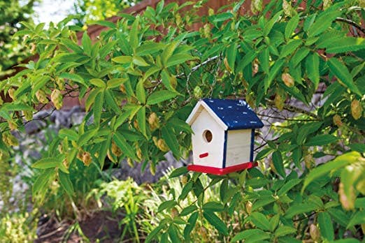 Decorative birdhouse on a tree branch with green leaves and yellow fruit.
