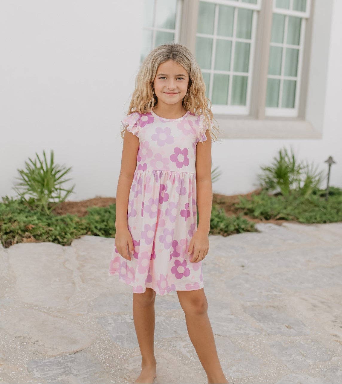 Young girl wearing a pink floral dress standing outdoors.
