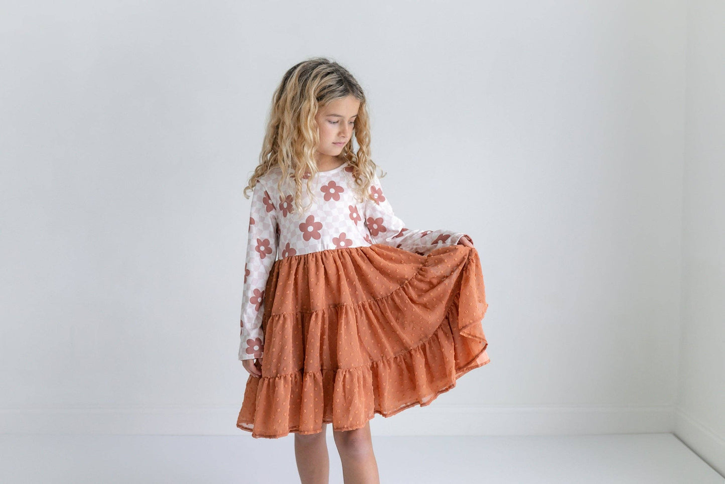 Young girl wearing a floral top and rust-colored skirt against a white background