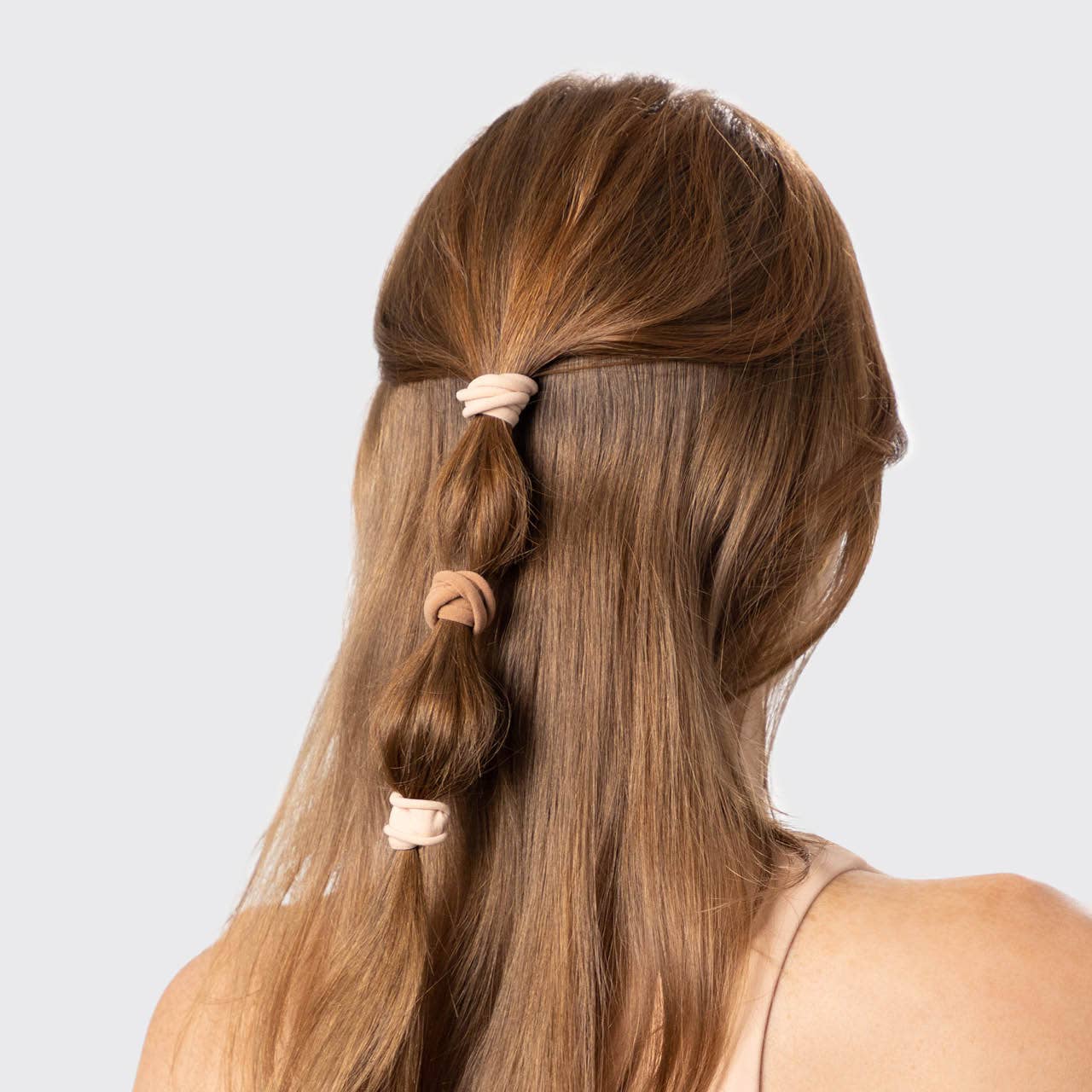 Long brown hair styled in a side braid with pink hair ties on a light gray background