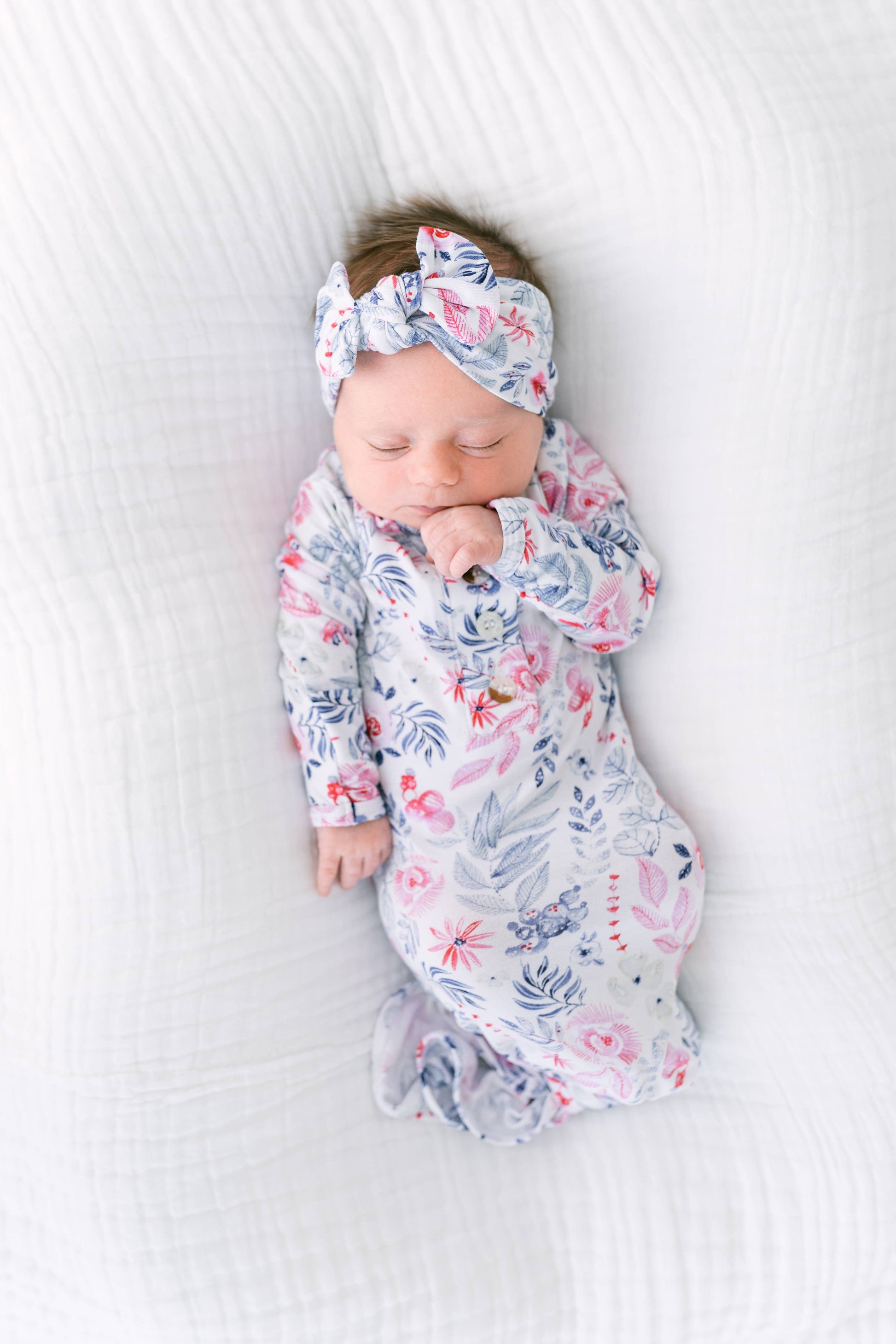 Newborn baby swaddled in a floral blanket with a matching headband on a white background